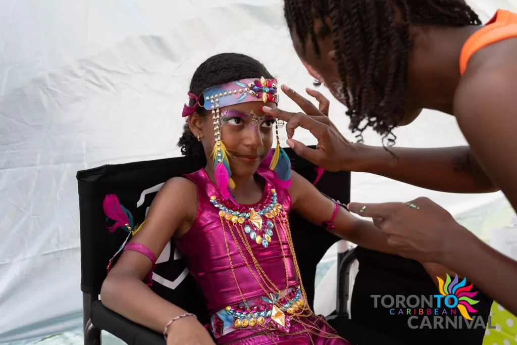 junior carnival reveler prepares in her costume having make-up applied