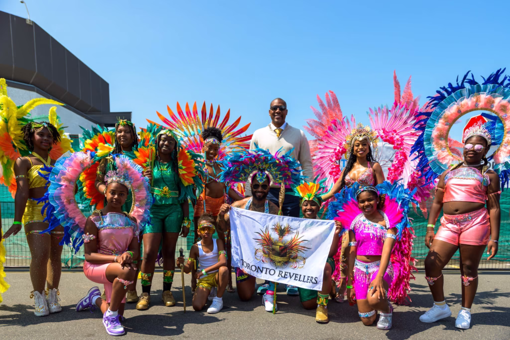 Toronto Revellers mas band group photo with members in colorful feathered carnival costumes at 2025 carnival launch
